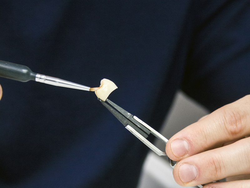 Technician applying ceramic to a crown held in tweezers